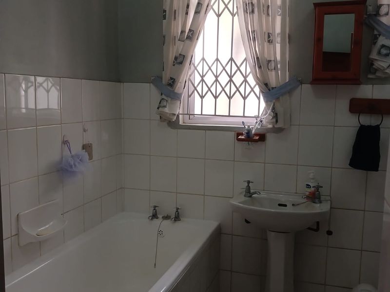 A functional bathroom featuring a standard bathtub, pedestal basin, and ceramic tiling throughout, with a security gate fitted to the window.
