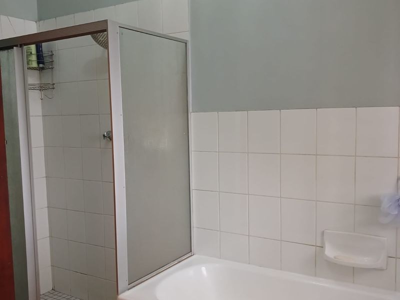 A functional bathroom featuring a built-in bathtub and a separate shower enclosure with tiled finishes.