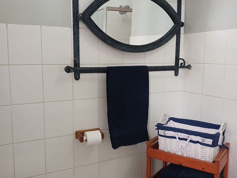 A functional bathroom featuring white wall tiles, tiled flooring, and a decorative wall-mounted mirror with integrated shelving.