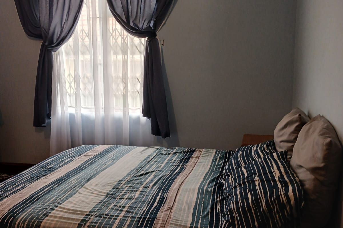 A bedroom featuring a window with a security gate, decorative cornice, and wall-mounted air vent.
