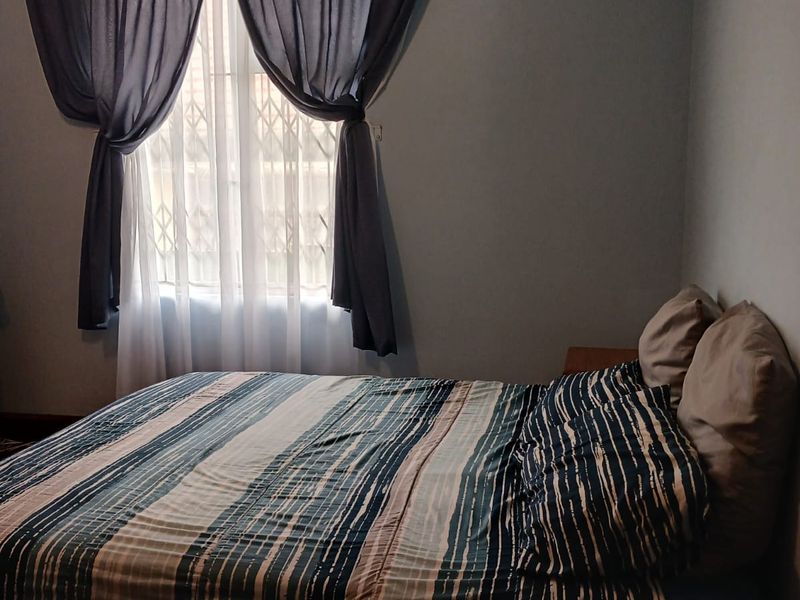 A bedroom featuring a window with a security gate, decorative cornice, and wall-mounted air vent.
