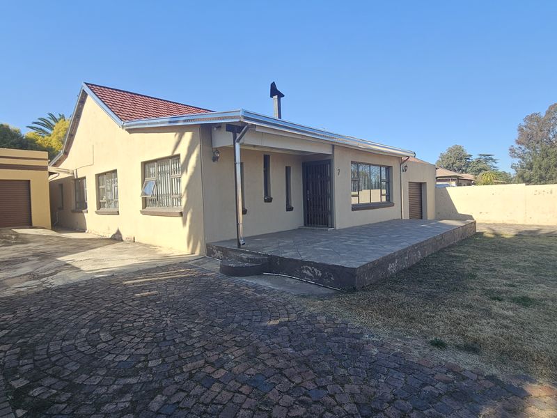 Front view of a single-story house featuring a paved driveway, attached garage, covered patio, and perimeter walling on a spacious plot.