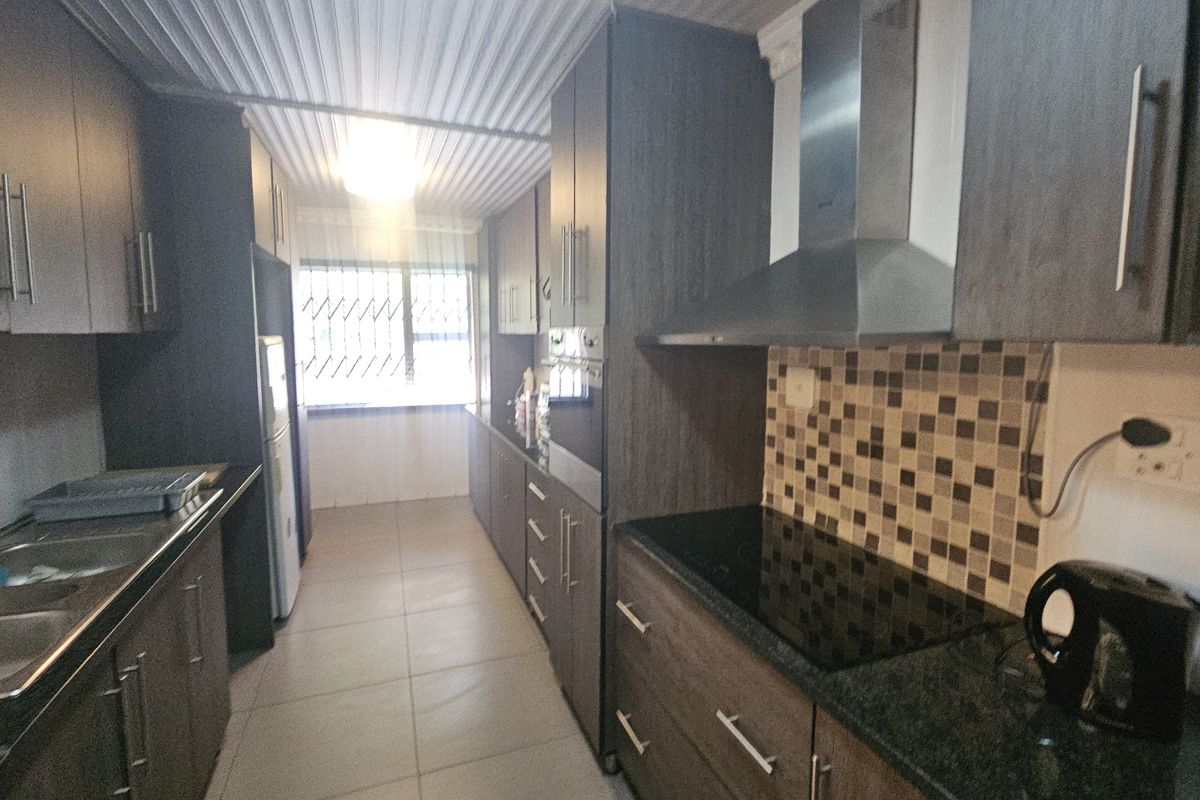 Modern galley-style kitchen featuring dark wood cabinetry, granite countertops, integrated electric hob, extractor fan, and tiled backsplash with ample storage space.