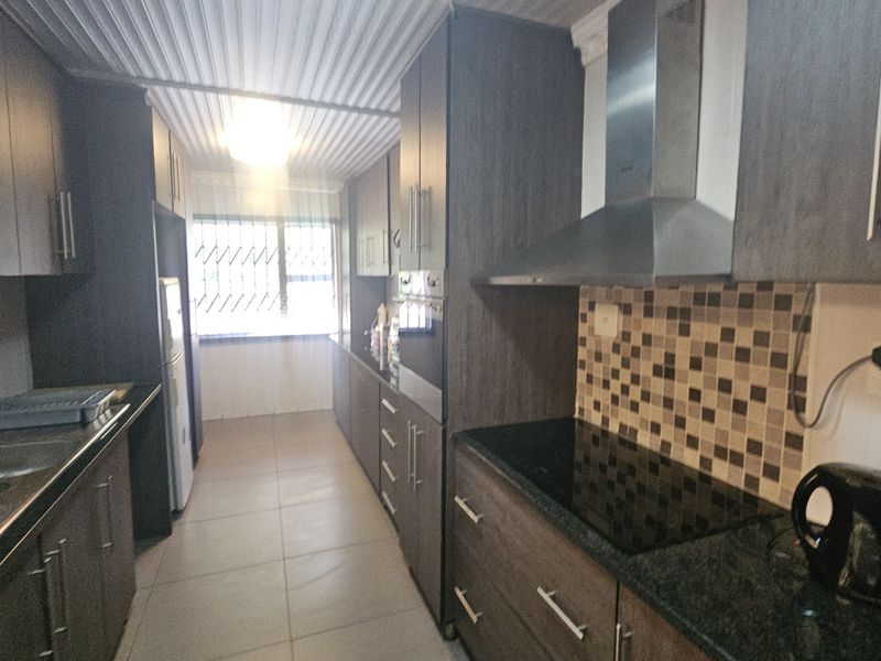 Modern galley-style kitchen featuring dark wood cabinetry, granite countertops, integrated electric hob, extractor fan, and tiled backsplash with ample storage space.