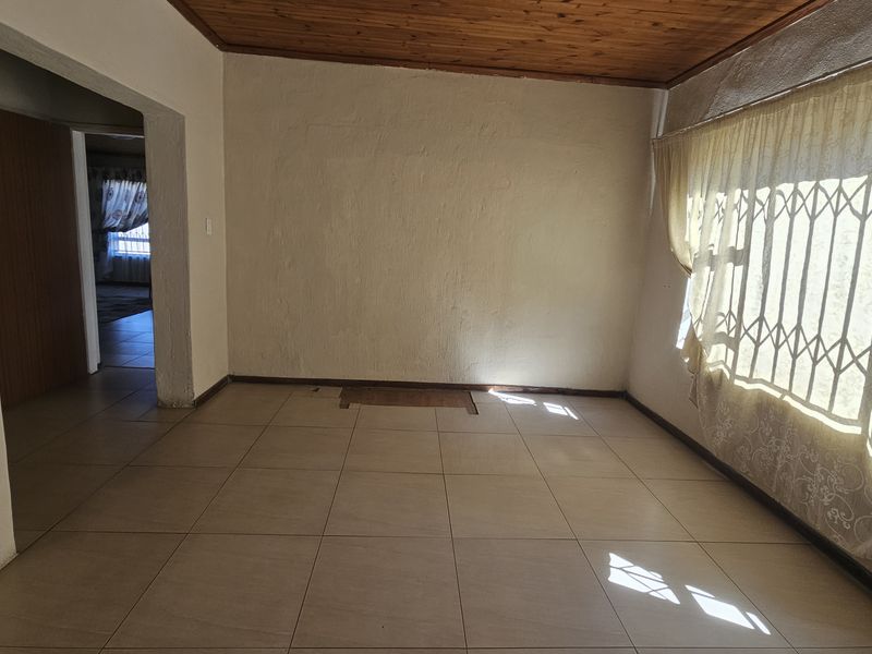 An empty living room featuring tiled flooring, a timber ceiling, and a security gate over the window, offering a blank canvas for renovation.