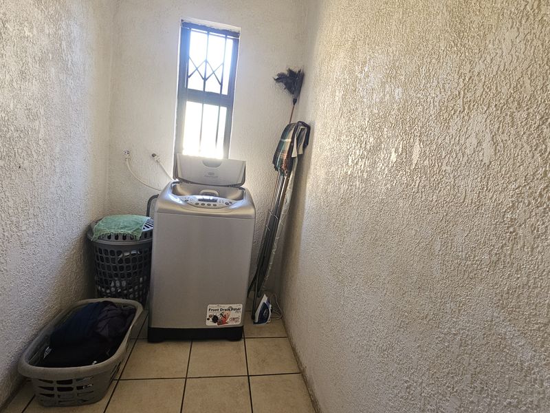 A functional laundry area featuring tiled flooring and a window with security bars, providing a dedicated space for washing and utility tasks.