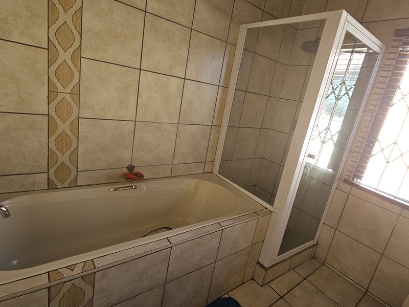 A functional bathroom featuring a built-in bathtub, a separate shower enclosure, and neutral ceramic tiling throughout.