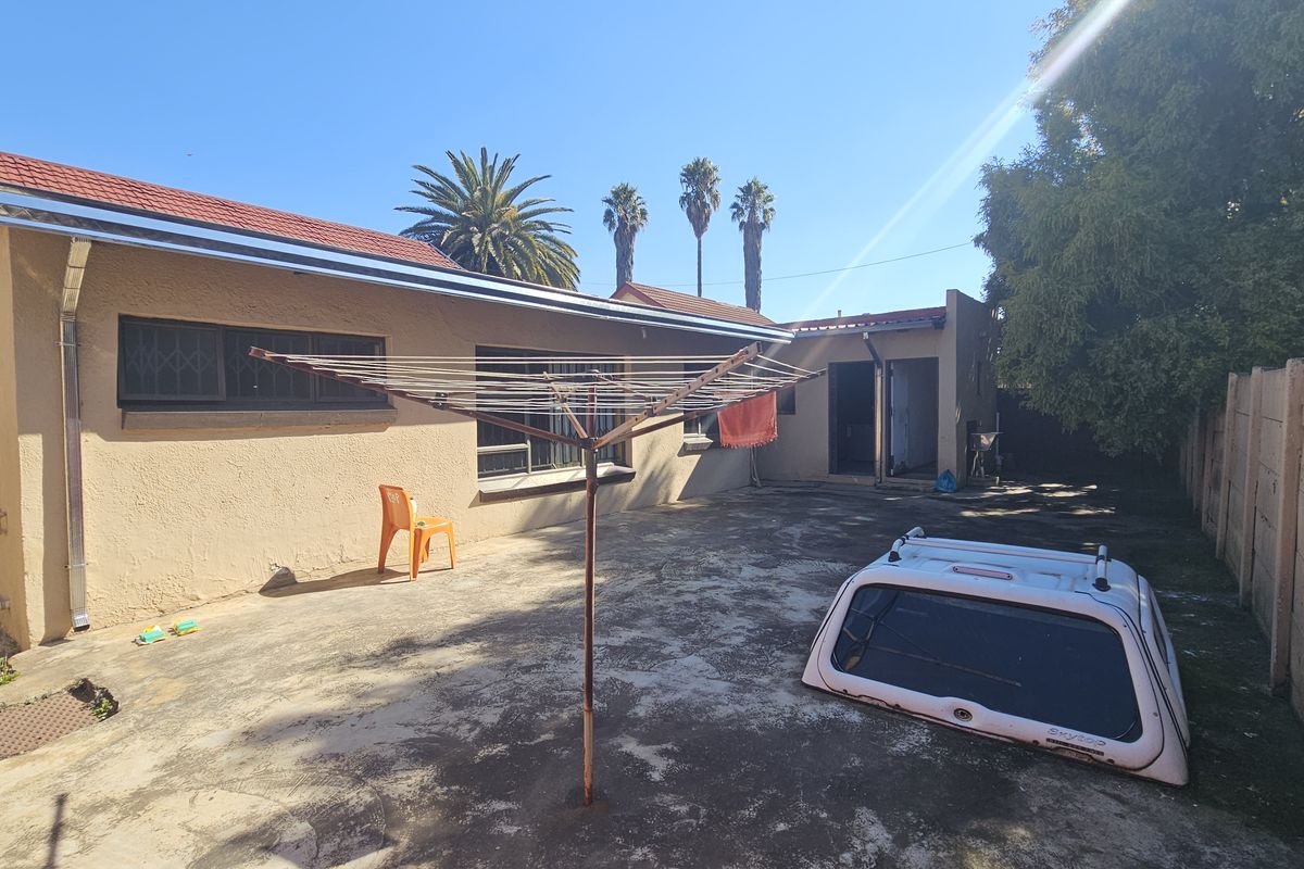 Rear exterior view of the property featuring a paved courtyard, tiled roof, and precast concrete boundary wall.