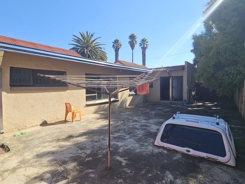 Rear exterior view of the property featuring a paved courtyard, tiled roof, and precast concrete boundary wall.