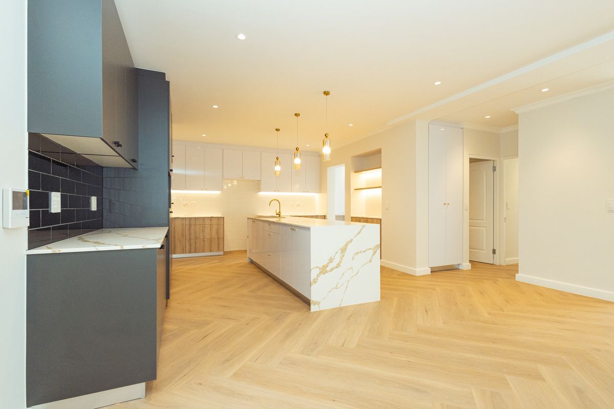 Modern, high-end kitchen featuring a large stone-topped island, herringbone timber flooring, sleek cabinetry, and elegant pendant lighting in a bright, open-plan space.