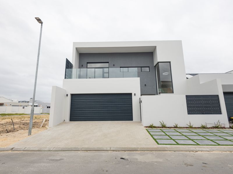 Modern double-story residential facade featuring a sleek automated garage, glass-fronted balcony, and contemporary paved driveway with integrated landscaping.