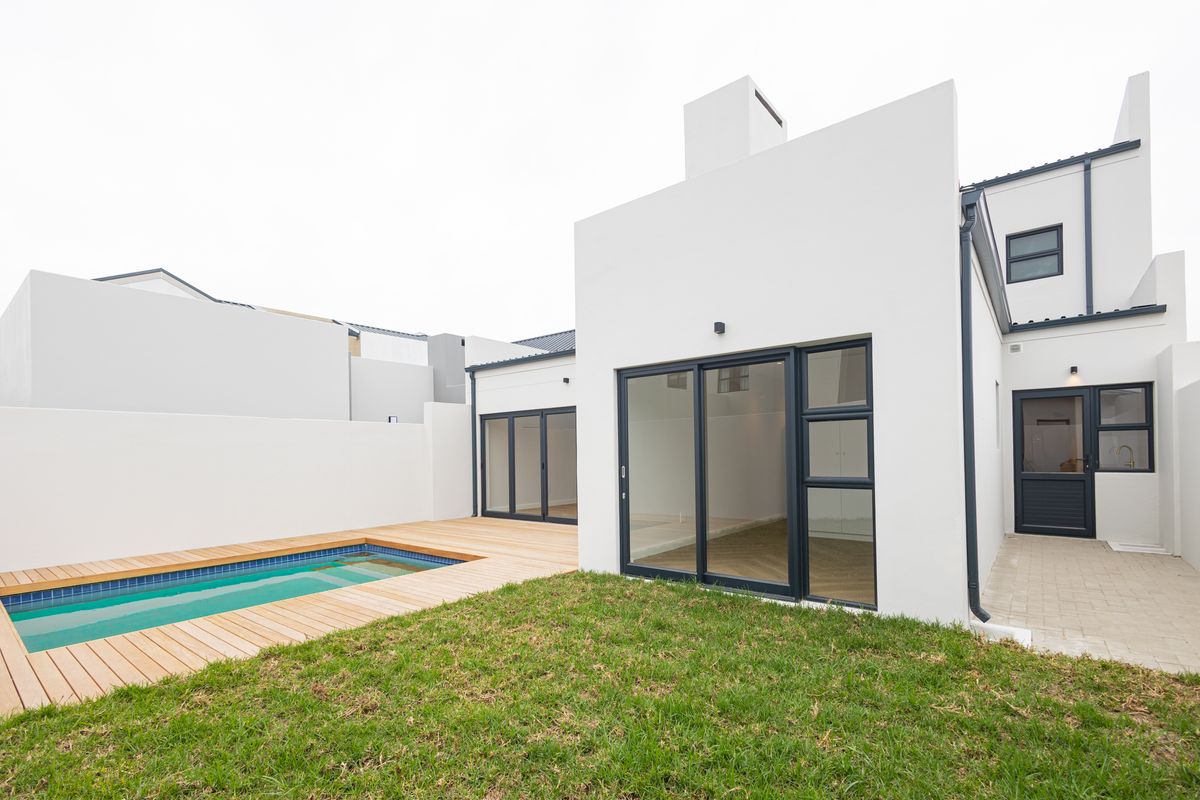 Rear view of a modern home featuring a swimming pool with timber decking, a small lawn, and large sliding glass doors.