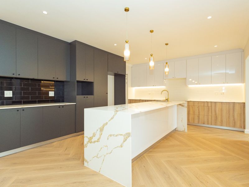 Modern, high-end kitchen featuring a large quartz island, two-tone cabinetry, herringbone flooring, and integrated lighting for a sleek, contemporary finish.