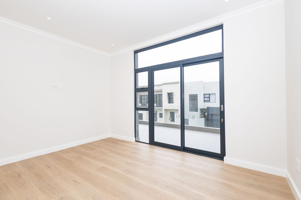 A bright, empty living room featuring modern laminate flooring, recessed lighting, and a large sliding glass door providing access to an outdoor balcony.
