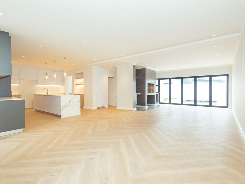 Spacious open-plan living area featuring modern kitchen with stone island, herringbone timber flooring, built-in fireplace, and large bi-fold doors opening to the exterior.
