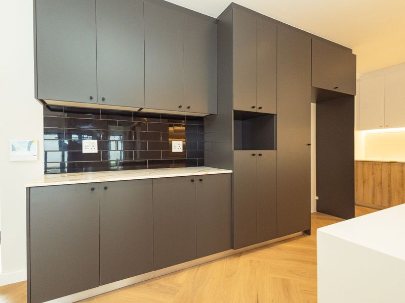 Modern kitchen featuring sleek dark grey cabinetry, stone countertops, a dark subway tile backsplash, and elegant herringbone timber flooring.