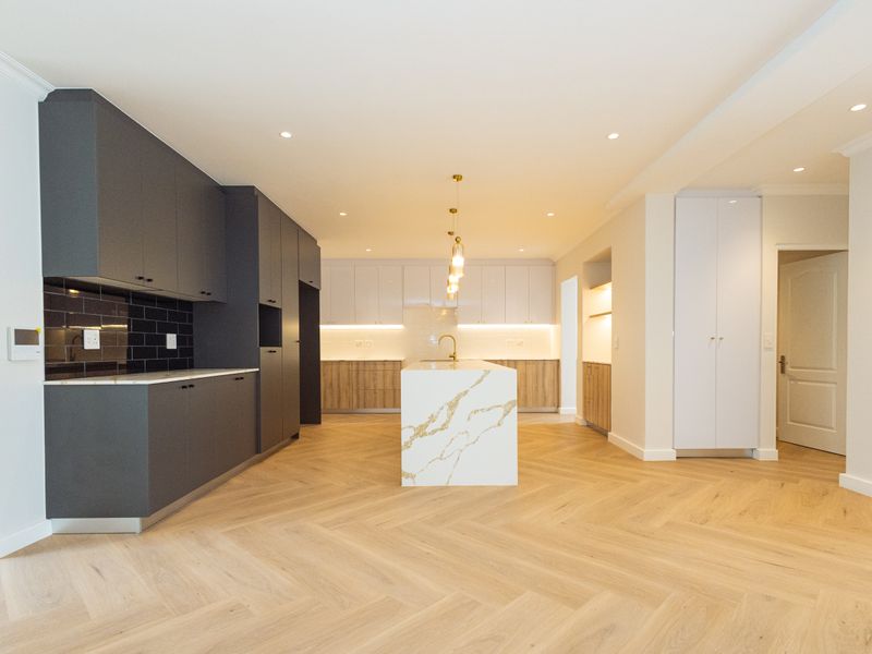 Modern, spacious kitchen featuring a central stone island, herringbone timber flooring, sleek two-tone cabinetry, and high-end finishes throughout.