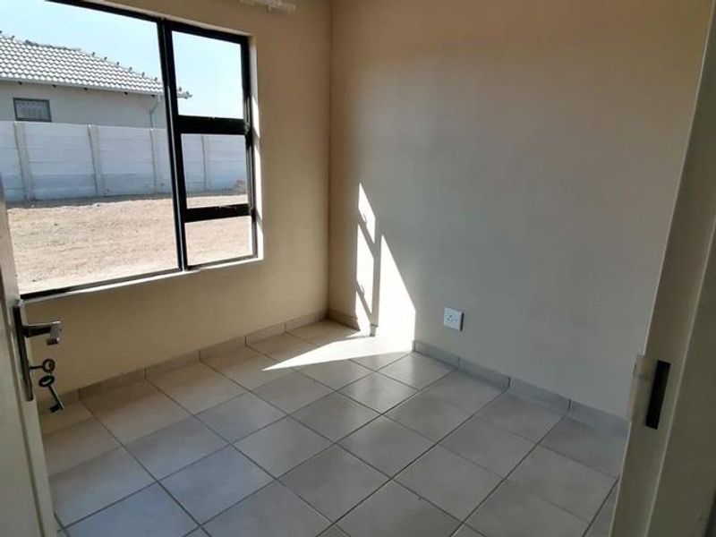An empty bedroom featuring neutral wall paint, tiled flooring, and a large aluminium-framed window providing natural light.