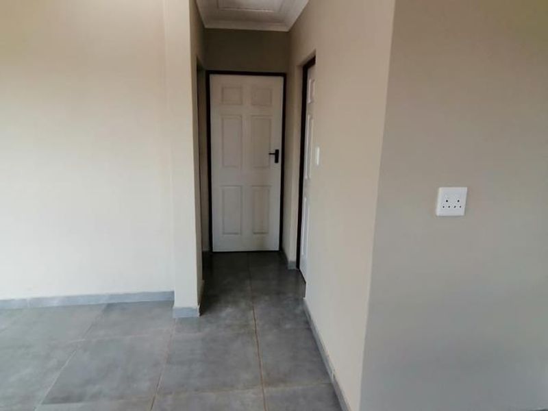 A clean, neutral-toned hallway featuring large format floor tiles, panelled interior doors, and a coved ceiling, providing a simple transition between living spaces.