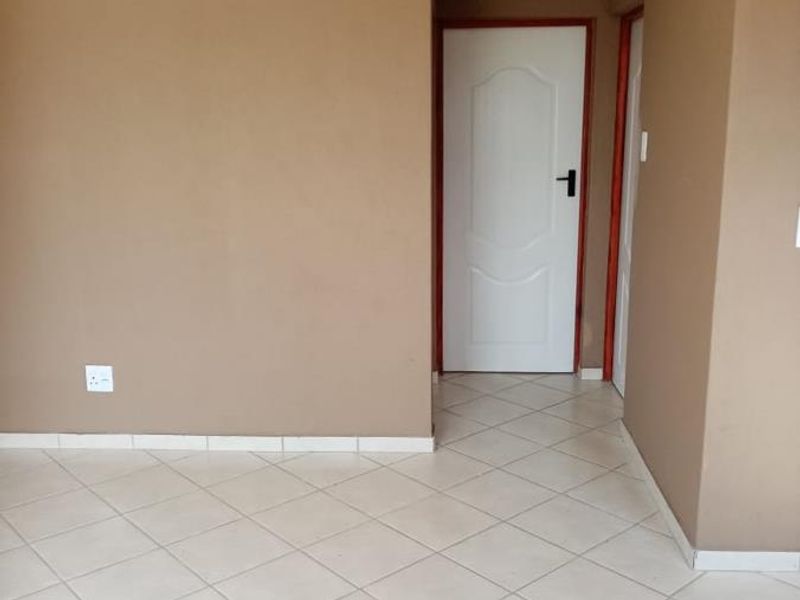 A clean, empty hallway featuring neutral wall tones, tiled flooring, and white internal doors, providing a simple transition space within the home.