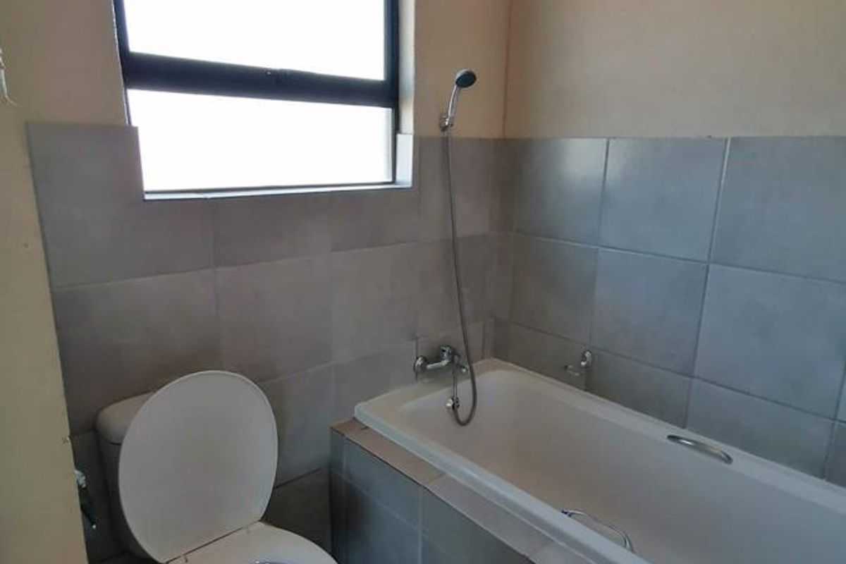 A functional bathroom featuring a bathtub with a handheld shower attachment, a toilet, and neutral wall tiling.