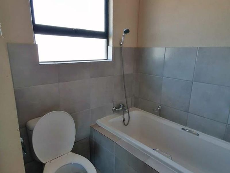 A functional bathroom featuring a bathtub with a handheld shower attachment, a toilet, and neutral wall tiling.