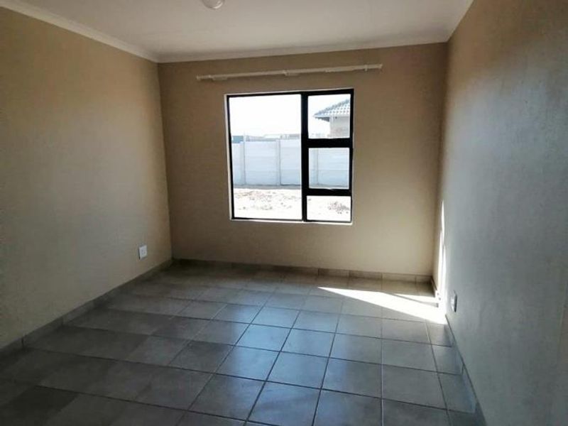 A clean, empty bedroom featuring neutral wall paint, tiled flooring, and a large aluminium-framed window with an installed curtain rail.