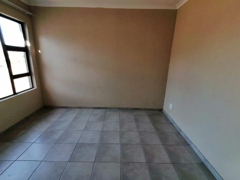 An empty bedroom featuring neutral wall paint, tiled flooring, and an aluminium-framed window, providing a blank canvas for personalization.