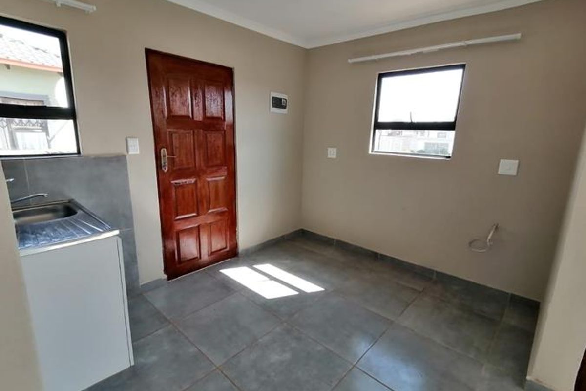 A functional scullery or utility area featuring tiled flooring, a stainless steel sink, and direct exterior access.