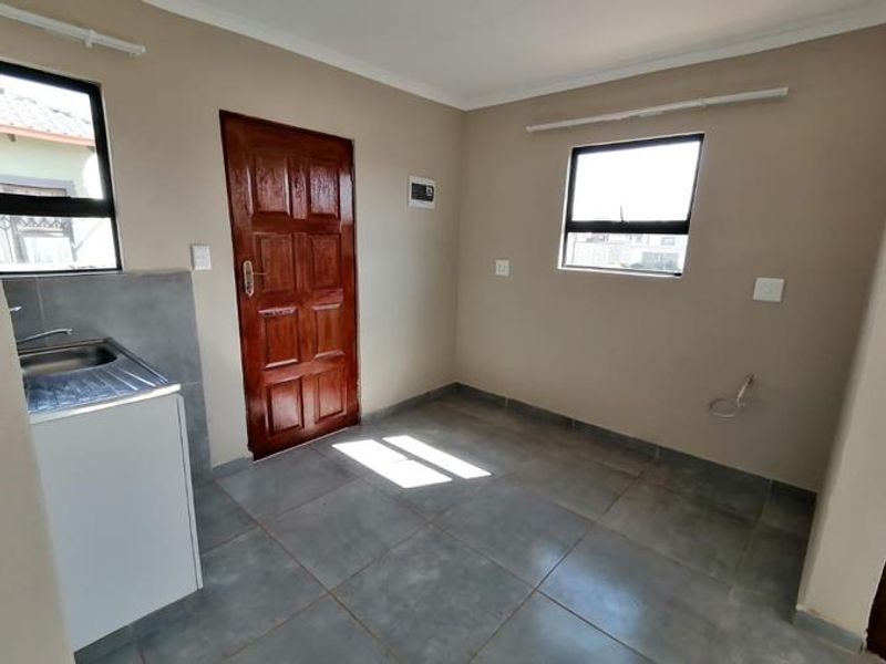 A functional scullery or utility area featuring tiled flooring, a stainless steel sink, and direct exterior access.