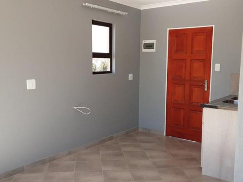A clean, empty kitchen area featuring tiled flooring, neutral grey walls, a timber door, and basic cabinetry with a sink.