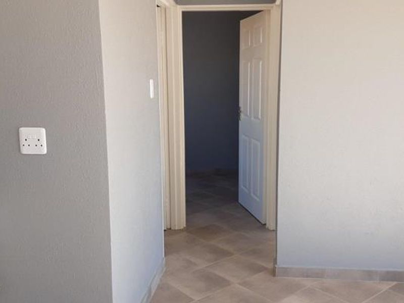 A clean, neutral-toned hallway featuring tiled flooring and internal doors, providing access to adjacent rooms within the property.