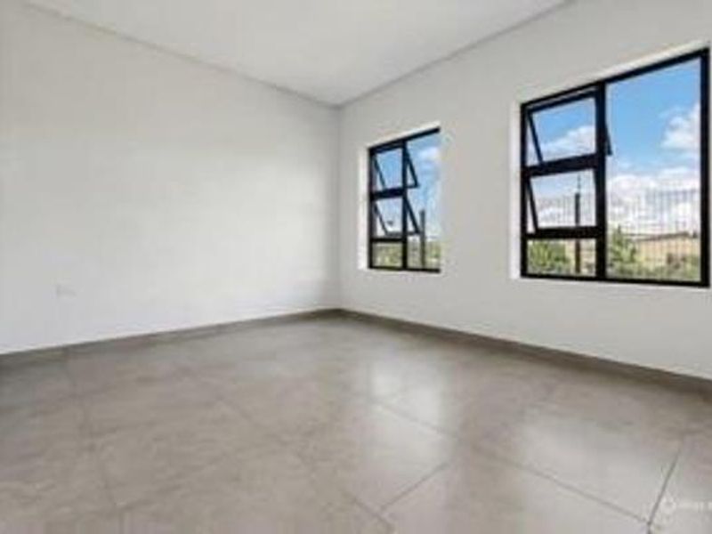A bright, empty bedroom featuring modern tiled flooring and large aluminium-framed windows that provide ample natural light.