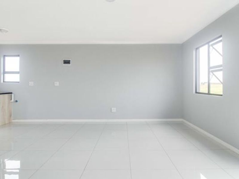 A bright, empty open-plan living area featuring neutral grey walls, polished white floor tiles, and modern casement windows.