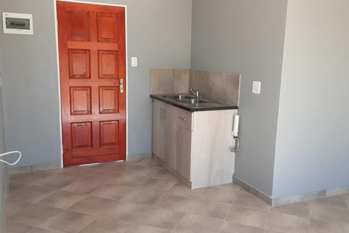 A compact kitchen area featuring built-in cabinetry, a stainless steel sink, and tiled flooring, providing a functional space for basic food preparation.