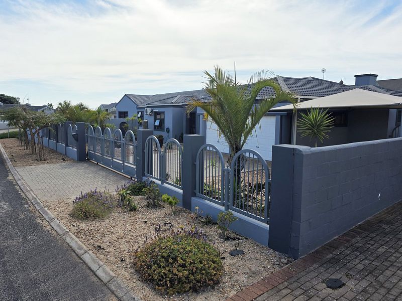 Front exterior view of a modern house featuring a grey painted facade, secure metal fencing, a paved driveway, and a tiled roof.