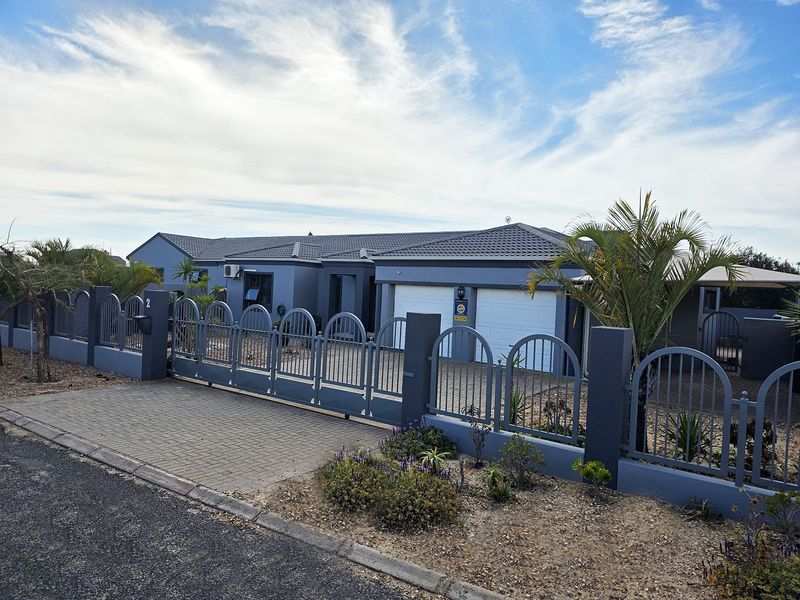 Front elevation of a modern single-story house featuring a paved driveway, double garage, and secure metal perimeter fencing.