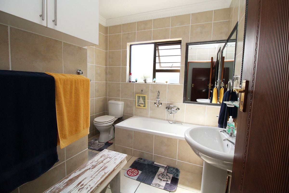 A functional bathroom featuring a pedestal basin, built-in bathtub, toilet, and neutral wall tiling with a window for natural light.