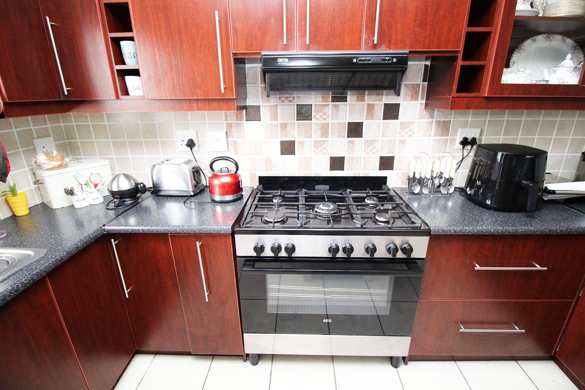 A functional kitchen featuring dark wood cabinetry, a gas stove with oven, extractor fan, and tiled backsplash with neutral countertops.