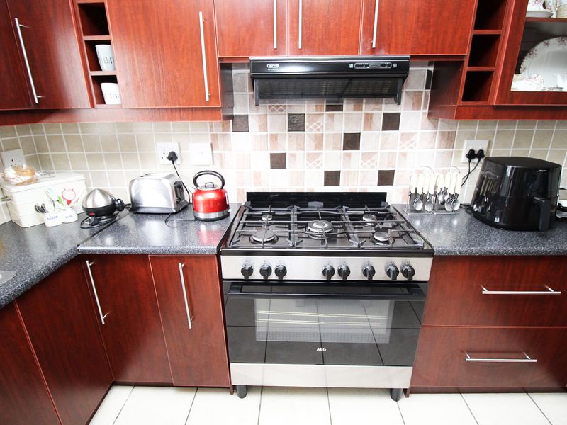 A functional kitchen featuring dark wood cabinetry, a gas stove with oven, extractor fan, and tiled backsplash with neutral countertops.