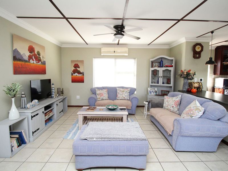 An open-plan living area featuring tiled floors, a ceiling fan, and a split-system air conditioner, seamlessly connected to a kitchen with breakfast bar seating.
