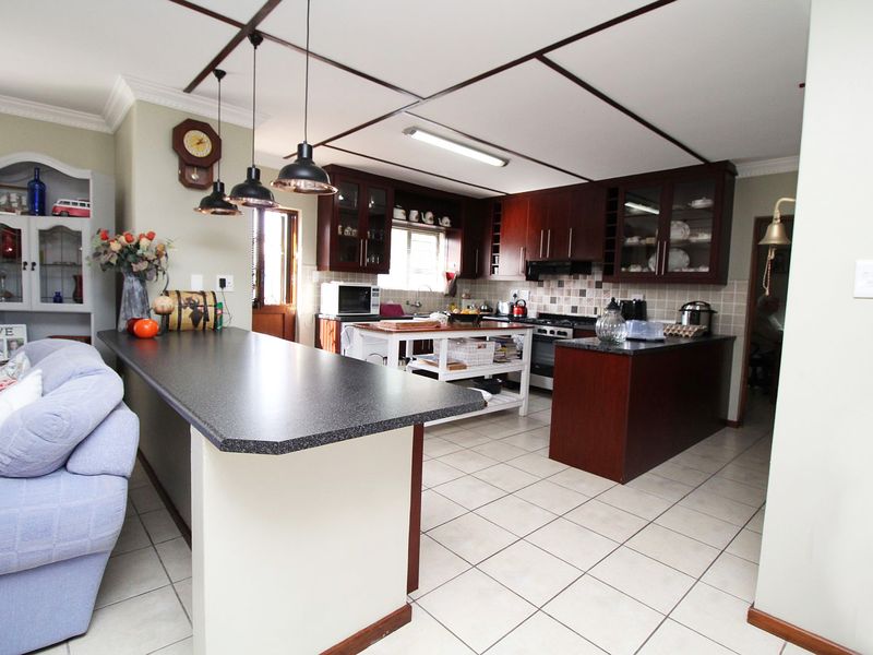 Open-plan kitchen featuring dark wood cabinetry, granite countertops, a breakfast bar, and tiled flooring, seamlessly connecting to the living area.