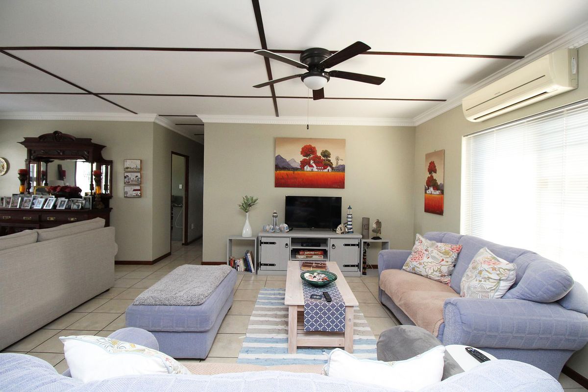 A comfortable living room featuring tiled flooring, a ceiling fan, and a wall-mounted split-system air conditioner.