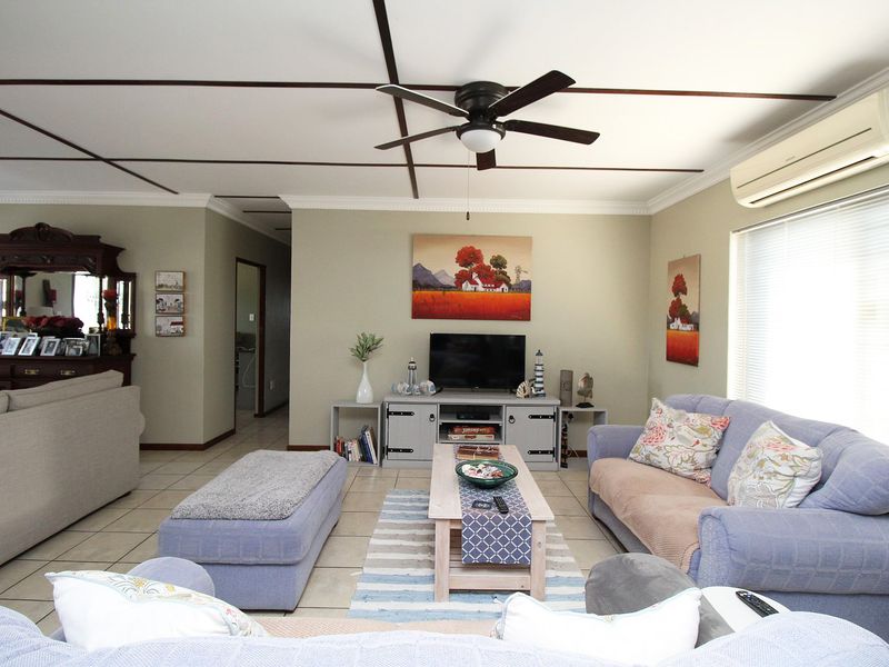 A comfortable living room featuring tiled flooring, a ceiling fan, and a wall-mounted split-system air conditioner.