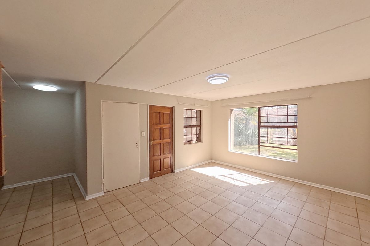 A bright, empty living area featuring neutral tiled flooring, a timber entrance door, and large steel-framed windows allowing for natural light.