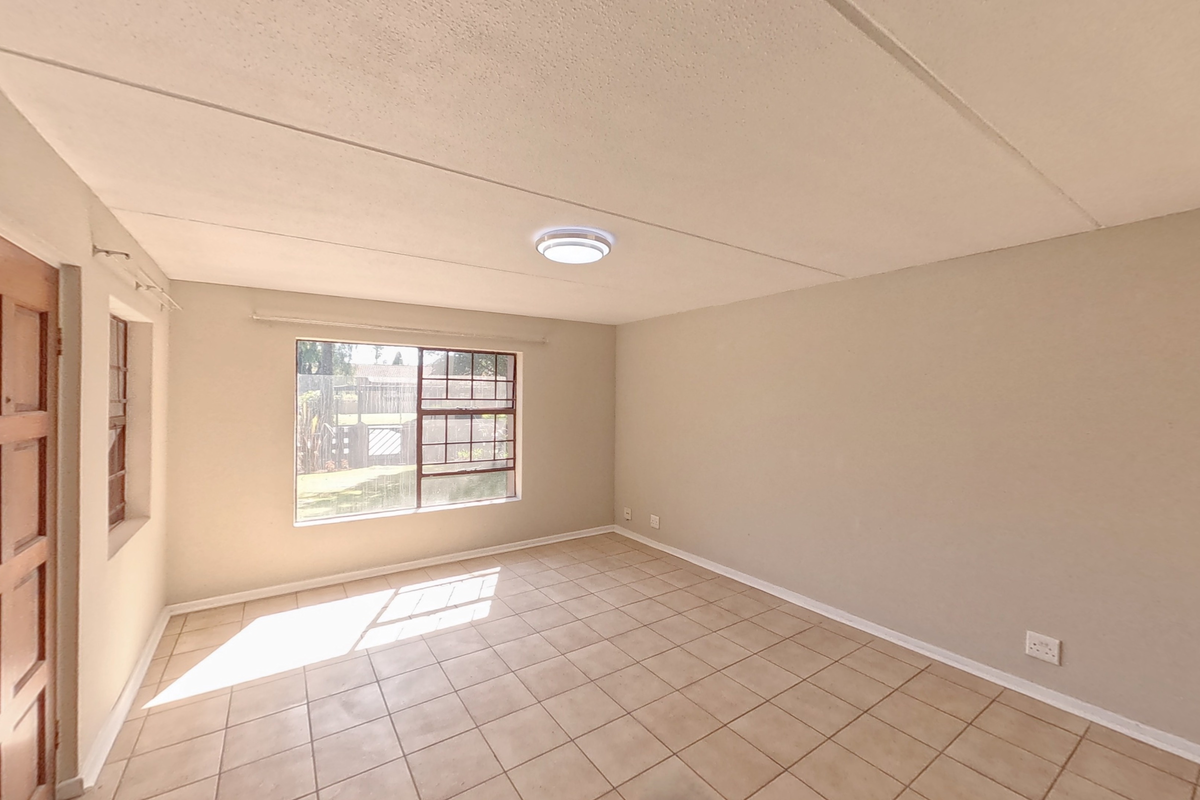 An empty bedroom featuring tiled flooring, steel-framed windows, and a ceiling-mounted light fixture, offering a blank canvas for potential renovation.