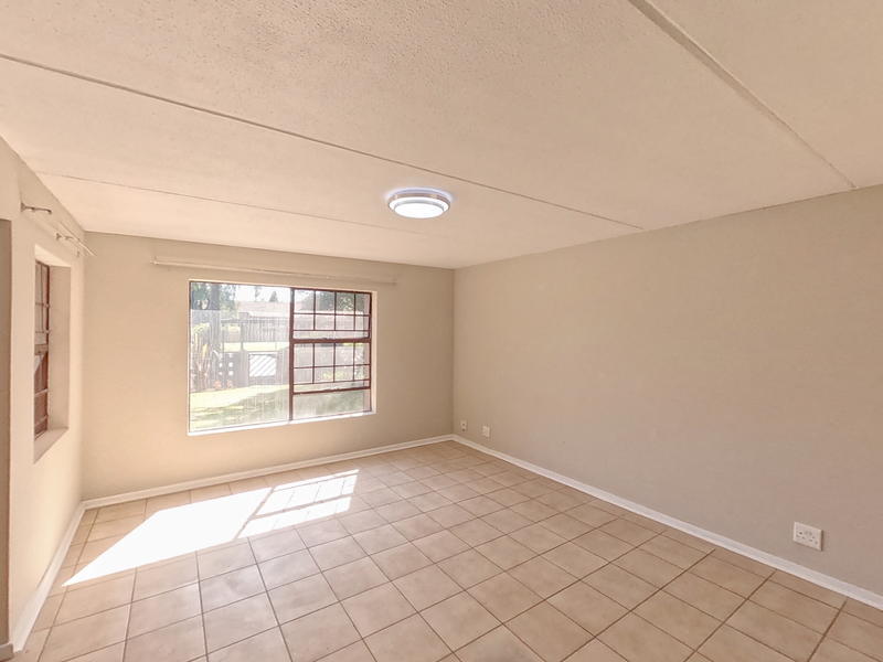 An empty bedroom featuring tiled flooring, steel-framed windows, and a ceiling-mounted light fixture, offering a blank canvas for potential renovation.