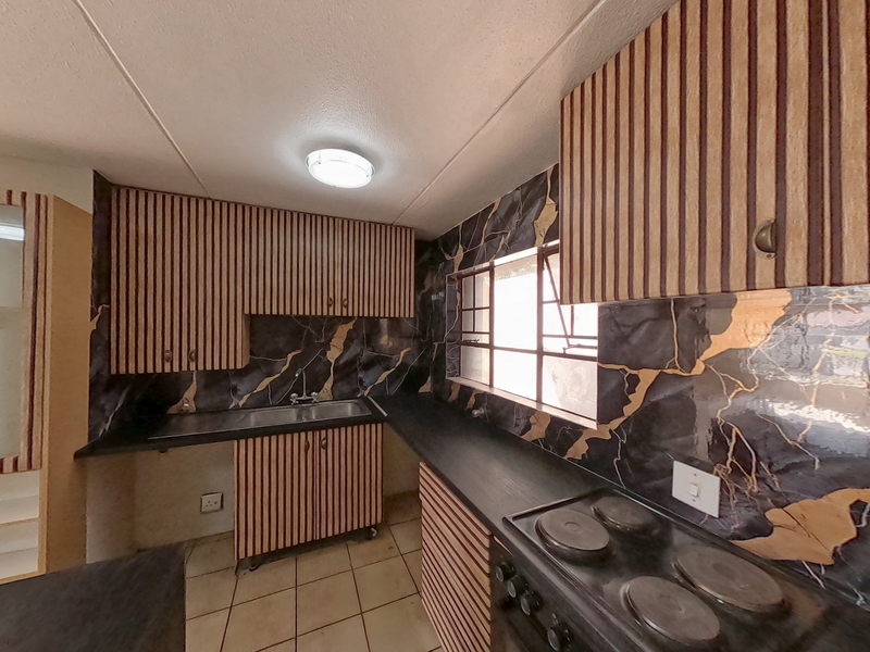A functional kitchen featuring built-in cabinetry, dark marble-effect backsplash, electric hob, and stainless steel sink, offering a dated aesthetic ready for modernization.