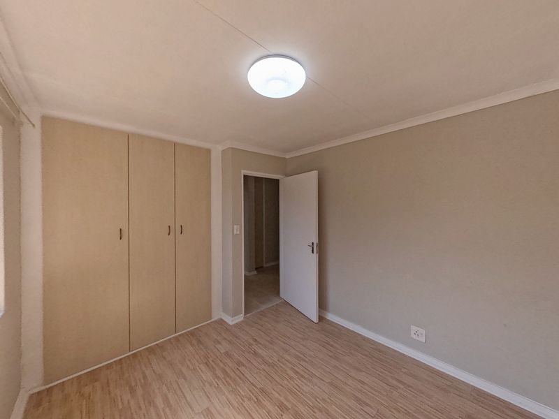 A clean, empty bedroom featuring laminate flooring, built-in cupboards, and neutral wall tones, offering a blank canvas for personalization.