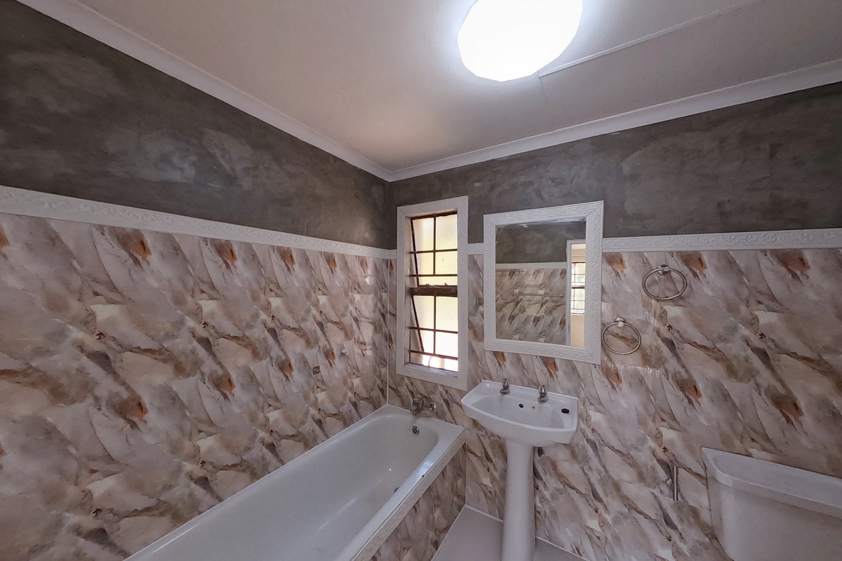 A bathroom featuring a bathtub, pedestal sink, and mirror, with partially finished wall surfaces and dated tiling throughout.